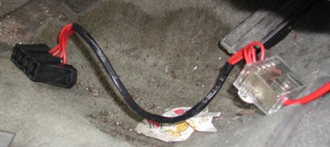 1988 Ford LTD Crown Victoria - Amplifier power wiring routed across a dirty gray carpeted vehicle floor: a black-loomed heavy-gauge cable splits into multiple red leads f…