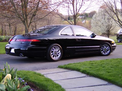 1996 Mercury Grand Marquis - A black coupe with chrome wheels is parked on a driveway in front of a house and trees.