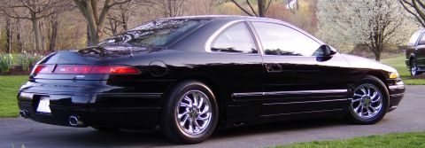 1996 Mercury Grand Marquis - A black coupe is parked on a driveway with trees and another vehicle in the background.