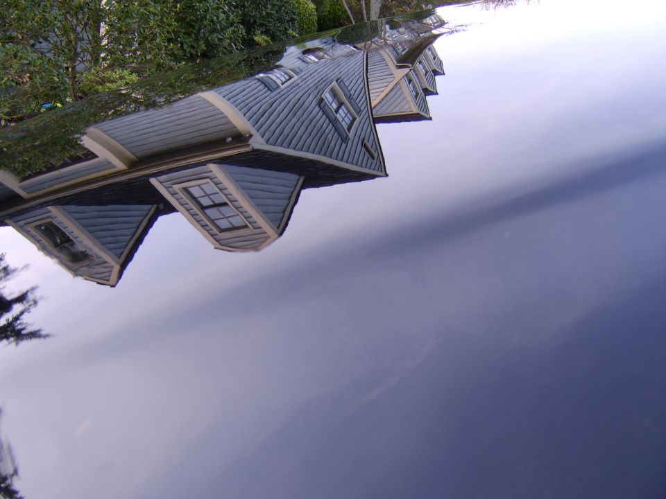 Gray two-story house and trees reflected in glossy dark blue vehicle paint
