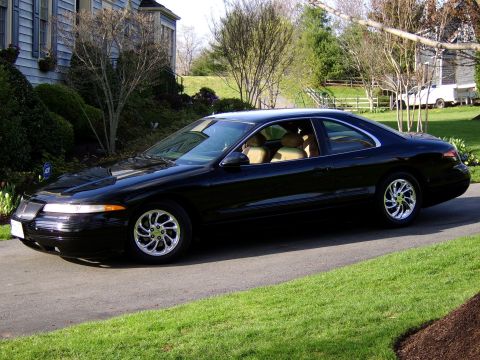 1996 Mercury Grand Marquis - A black coupe with a tan interior sits on a paved driveway in front of a house.