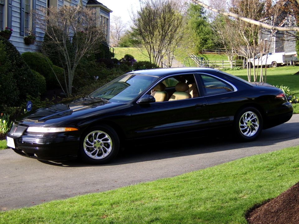 Black two-door luxury coupe with tan leather interior and chrome directional wheels in a driveway