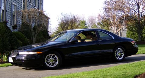 1996 Mercury Grand Marquis - A black coupe with chrome wheels is parked in front of a house.