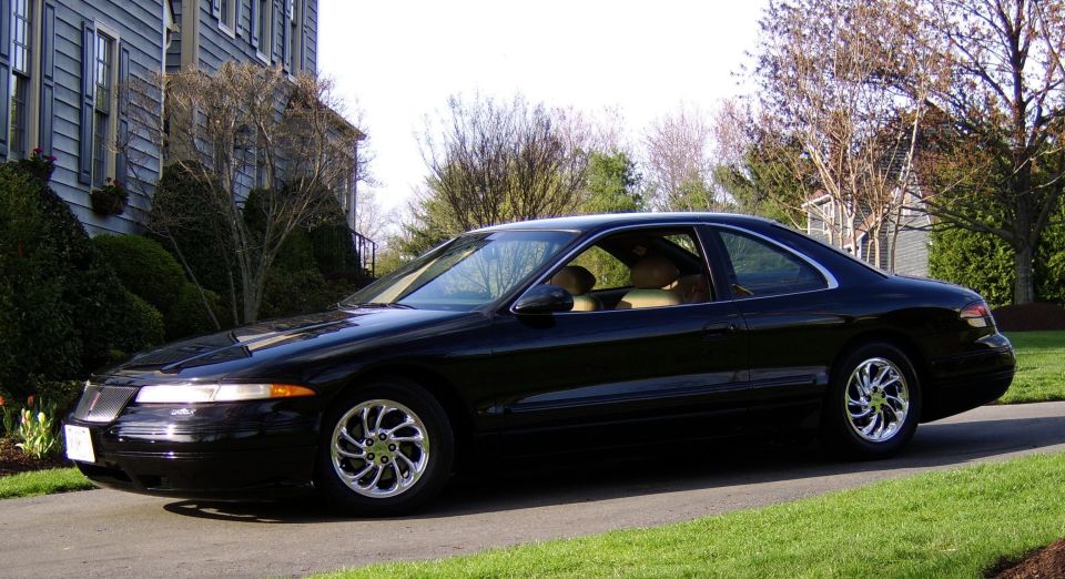 Black Lincoln Mark VIII coupe with chrome wheels and tan interior parked on a landscaped driveway