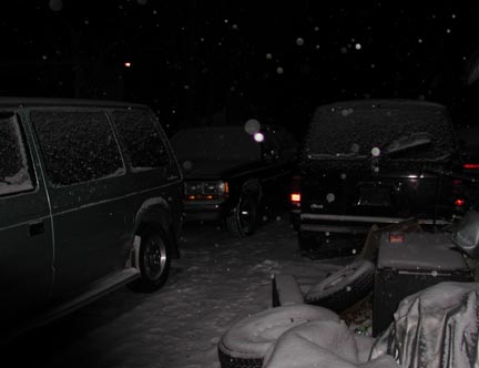 1988 Ford LTD Crown Victoria - Nighttime shot of a snow-covered driveway during falling snow, with a dark minivan or van at left, a boxy SUV in the middle background and…