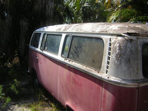 1971 Volkswagen Vanagon - A weathered red and white Volkswagen Type 2 van sits abandoned amongst overgrown vegetation.