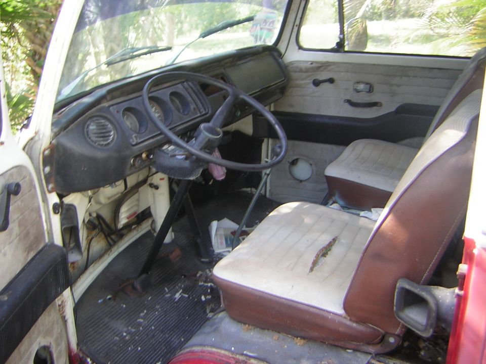 Worn interior of a vintage VW bus with large steering wheel and torn tan seats
