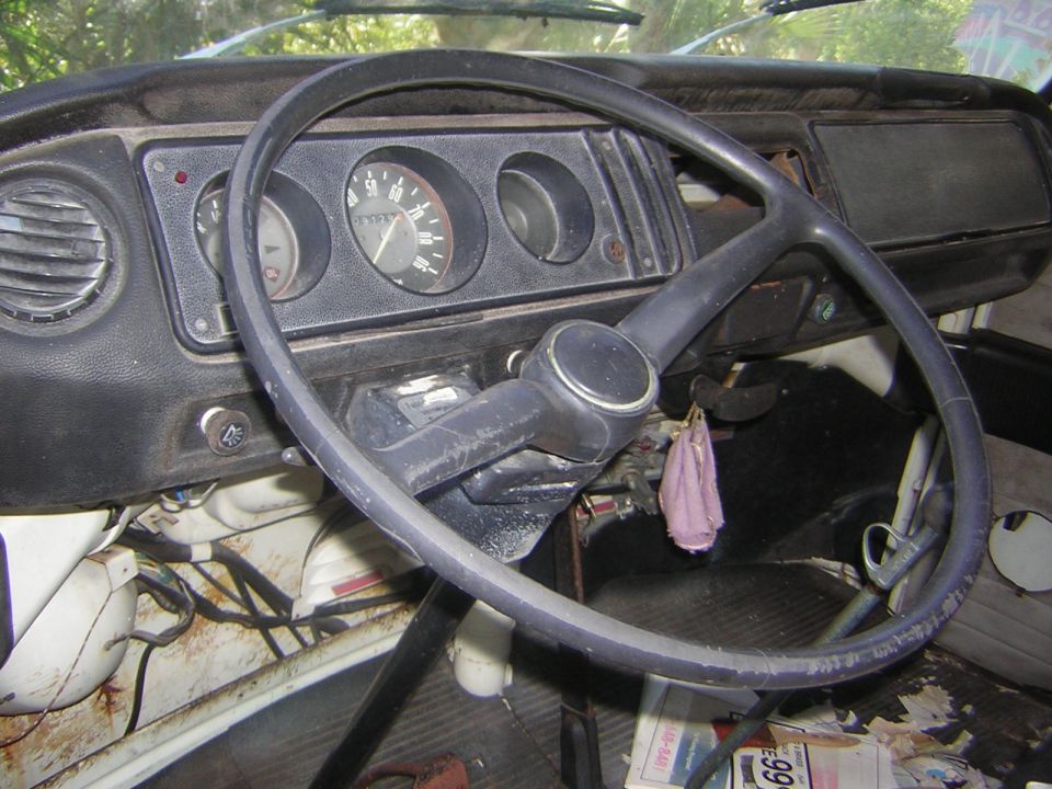 Weathered vintage car interior with thin black steering wheel and round analog gauges
