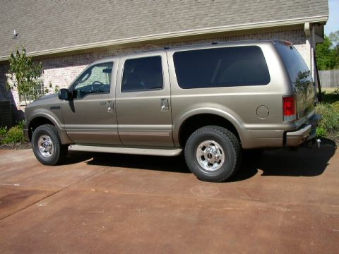 1995 Ford Bronco - This tan SUV is seen from the side, parked on a concrete driveway in front of a brick house.