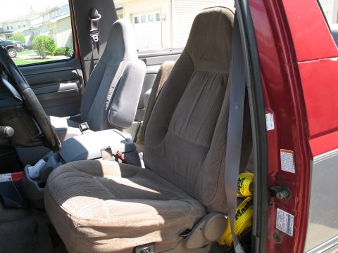 1995 Ford Bronco - Interior shot through the open passenger door of a red truck/SUV showing tan-brown cloth high-back bucket seats, the passenger seatback emb…