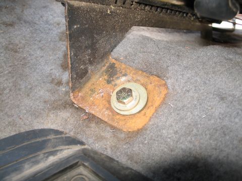 1995 Ford Bronco - Close-up of a rusted steel seat-mount bracket secured through a carpeted floorboard by a large hex bolt and washer, with the seat slider ra…