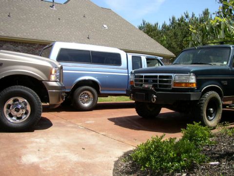 1995 Ford Bronco - Three Ford trucks are parked in a driveway in front of a house.