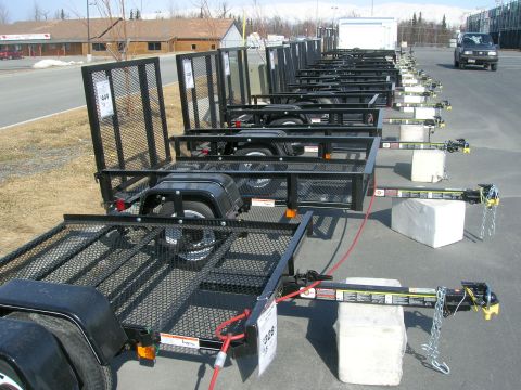 2003 Jeep TJ - Multiple black utility trailers are lined up in a parking lot, with a single SUV visible in the background.