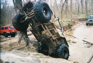 1992 Ford Bronco - An off-road vehicle is stuck on its side in a stream, with other vehicles in the background.