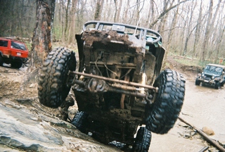 1992 Ford Bronco - An off-road vehicle is stuck on rocks, with other vehicles visible in the muddy terrain.