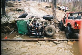 1992 Ford Bronco - Multiple off-road vehicles navigate a muddy, rocky terrain with one vehicle overturned.