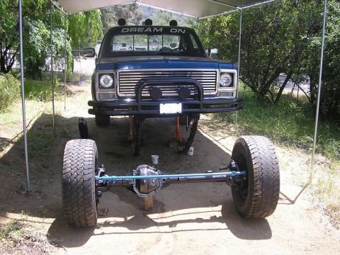 1979 Chevrolet C/K Pickup - This pickup truck is elevated on jacks with its front axle removed, revealing the undercarriage and large tires.
