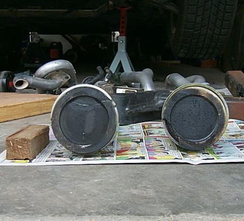 1988 Pontiac Fiero - Engine parts, including pistons and exhaust components, are laid out on newspaper.