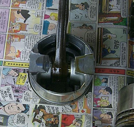 1988 Pontiac Fiero - A piston and connecting rod assembly rests on a surface covered with comic strips, with a SuperMotors.net watermark visible.