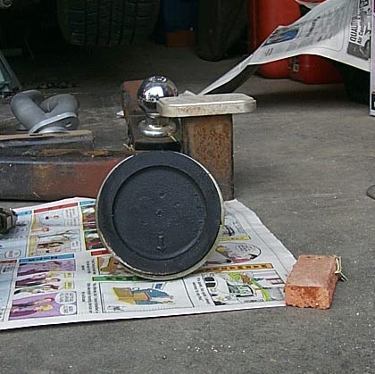 1988 Pontiac Fiero - Close-up of an unidentified automotive part laid out on a newspaper, with a hitch ball in the background.