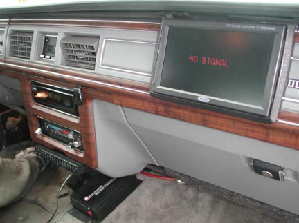 1988 Ford LTD Crown Victoria - Passenger side of a gray dash with woodgrain trim, retrofitted with a flip-out LCD monitor displaying "NO SIGNAL" in red text, plus two sta…