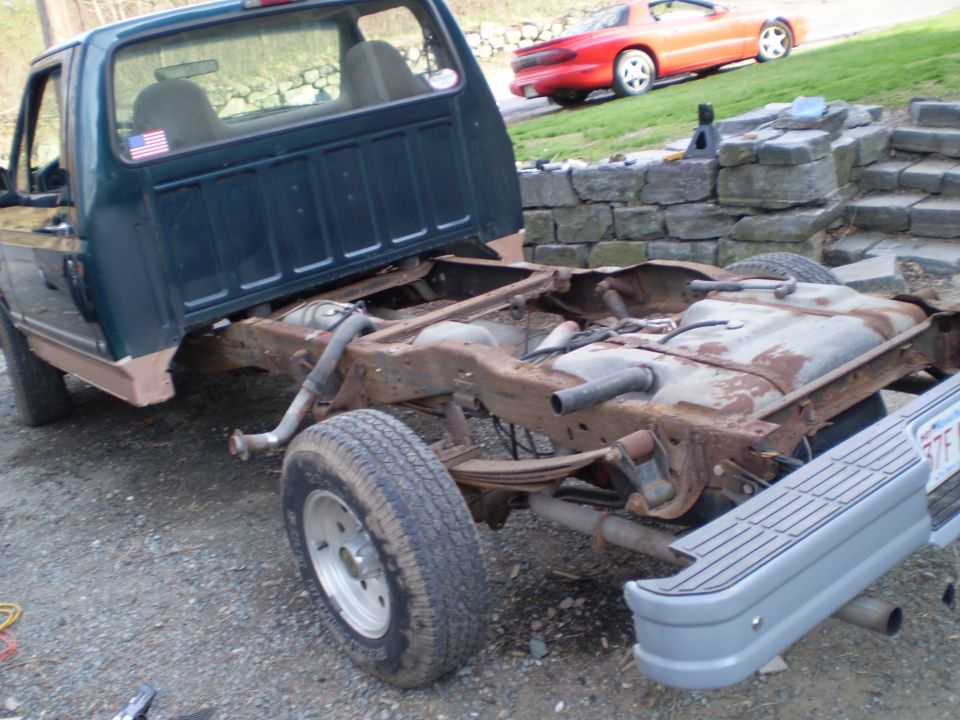 Green Ford F-150 truck chassis with rusty frame and fuel tank, viewed from the rear