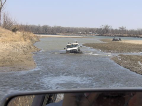 1992 Ford F-350 - A white pickup truck navigates a water crossing, with ATVs visible on the sandy bank.