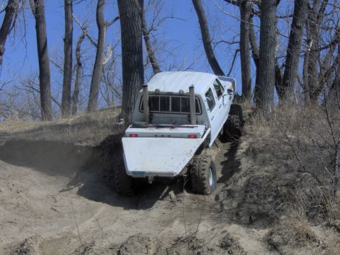 1992 Ford F-350 - This truck is navigating a steep, sandy incline surrounded by bare trees under a clear blue sky.