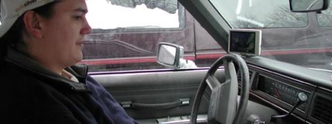 1988 Ford LTD Crown Victoria - View from the passenger seat of a car interior with gray cloth bench seats and a four-spoke steering wheel, showing two small aftermarket L…
