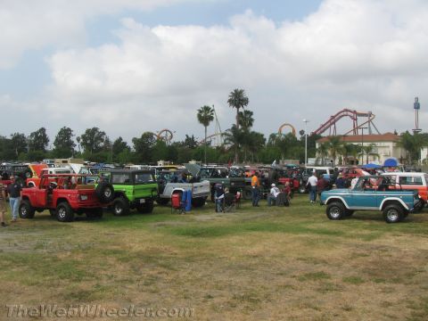 1968 Ford Mustang - A gathering of classic Ford Broncos and other vehicles is seen with a roller coaster and amusement park structures in the distance.