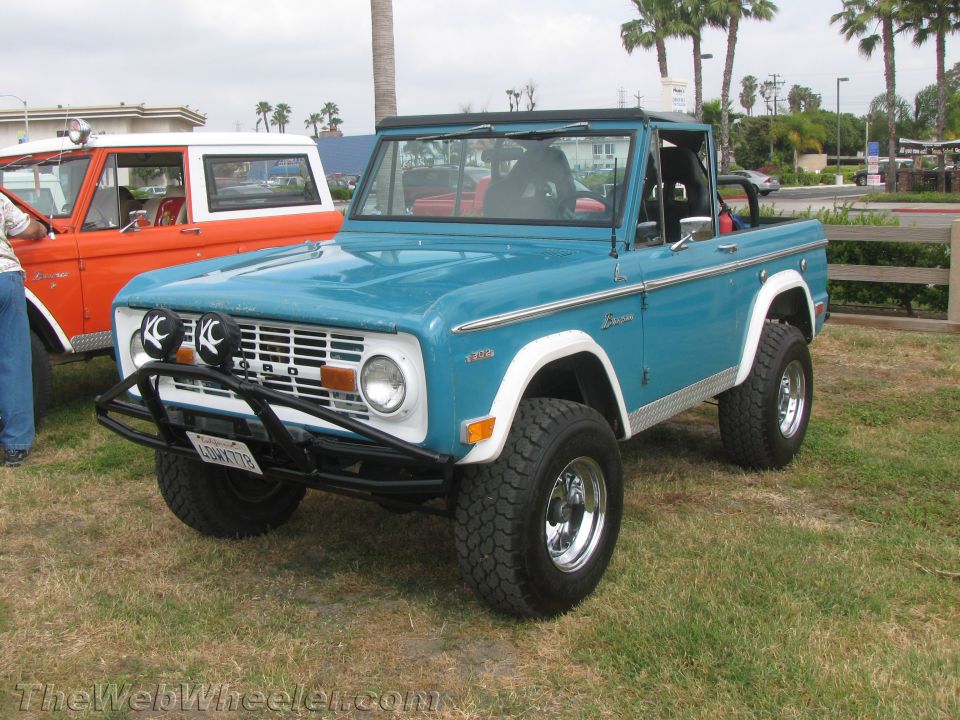 Blue 1968 Ford Bronco with white trim and a black bumper with KC lights, parked on grass