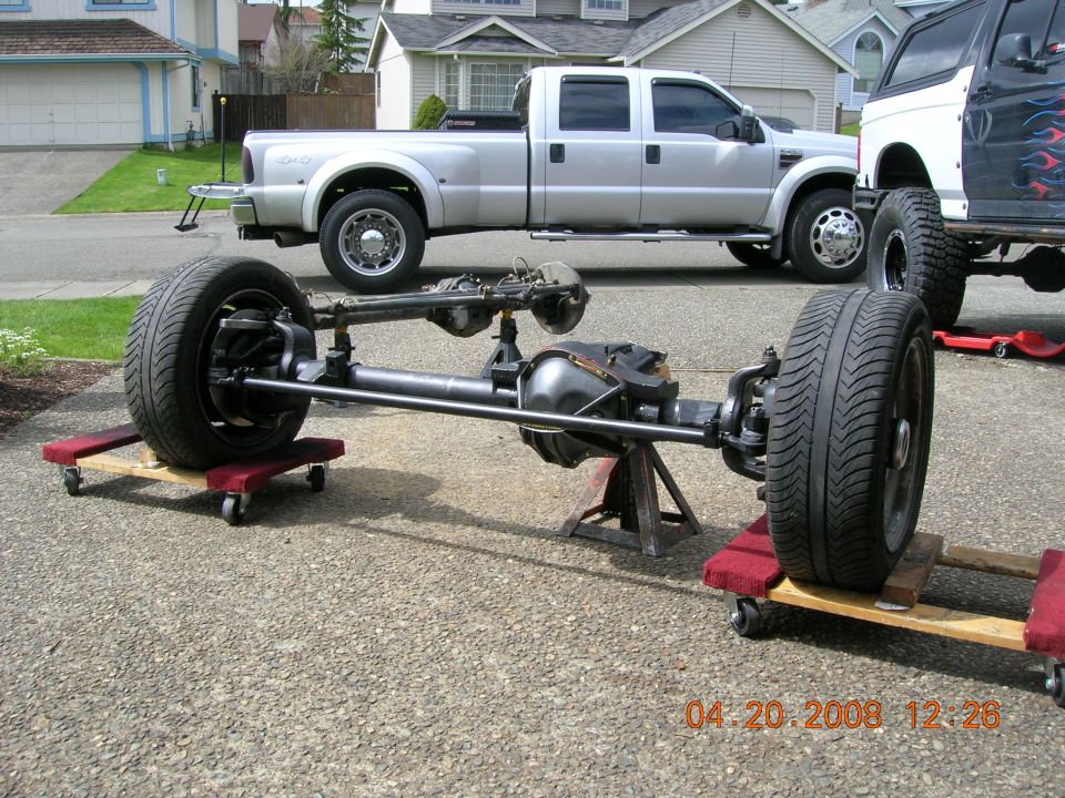 Front axle assembly on dollies with a silver pickup truck and a black SUV in the background