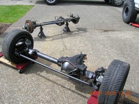 1996 Ford Bronco - Two vehicle axles, one on jack stands and the other on dollies, are displayed outdoors on a paved surface.