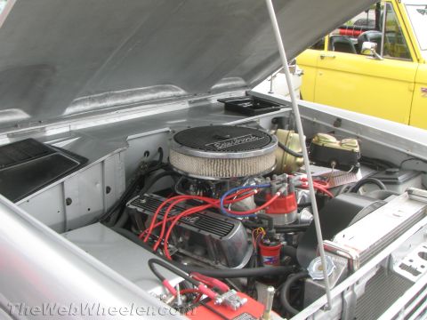 1968 Ford Mustang - The engine bay of a silver vehicle is open, with a yellow vehicle visible behind it.