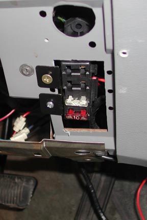 1988 Ford LTD Crown Victoria - Under-dash view of a small black fuse block screwed to a gray metal bracket, holding a red 10-amp blade fuse and a white in-line fuse holde…