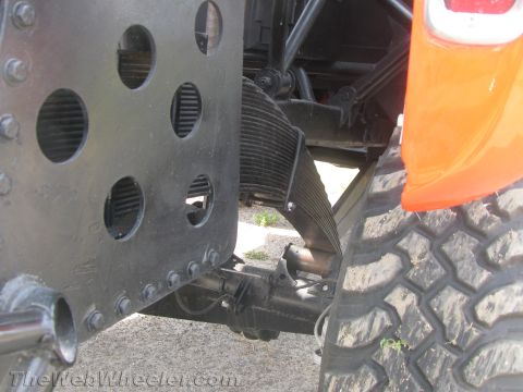 1968 Ford Mustang - Close-up view of the suspension and tire of an orange vehicle, with a black metal plate circular holes.