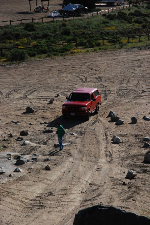 1995 Ford Bronco - A red 1995 Ford Bronco navigates a dusty, rocky terrain with tire tracks visible.