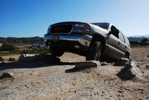 1995 Ford Bronco - GMC Yukon XL navigates rocky terrain under a clear blue sky.