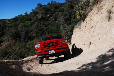 1995 Ford Bronco - A red 1992 Ford F-150 navigates a dusty trail under a clear blue sky.