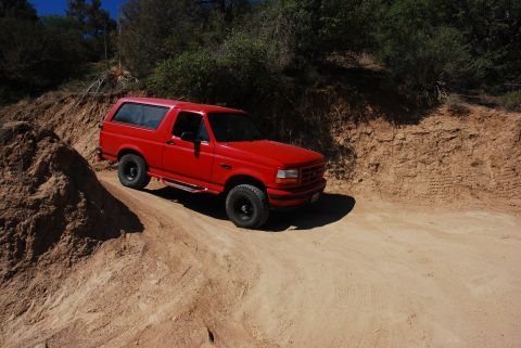 1995 Ford Bronco - A red SUV navigates a dusty, off-road trail under a clear blue sky.