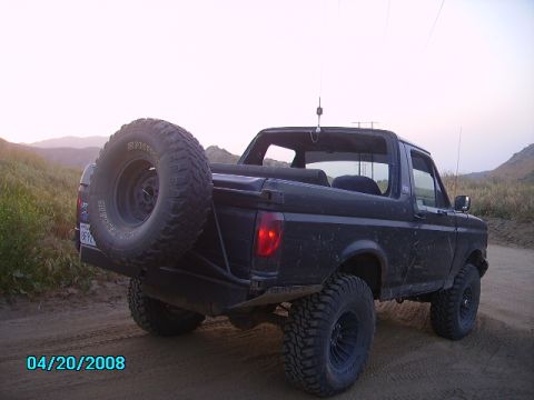 1990 Ford Bronco - Rear view of a 1990 Ford Bronco with a spare tire mounted on the back, parked off-road.