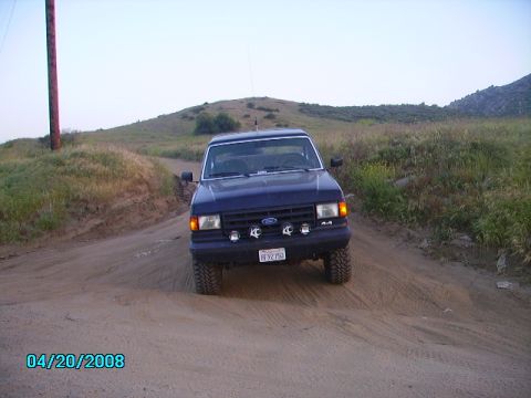 1990 Ford Bronco - A Ford truck is seen driving on a dusty, rural road with hills in the background.