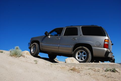 1995 Ford Bronco - Silver SUV navigates a rocky off-road trail under a bright blue sky.