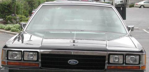 1988 Ford LTD Crown Victoria - Straight-on front view of a black Ford full-size sedan in a parking lot, cropped to the hood and grille. It has quad rectangular headlights…