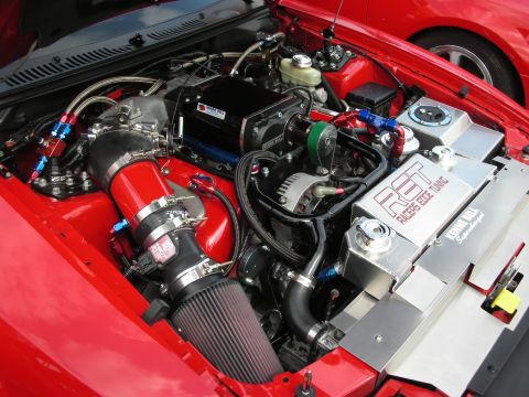 1992 Ford Crown Victoria - The engine bay of a modified vehicle, a supercharger and custom tuning components. Another red vehicle is partially visible.