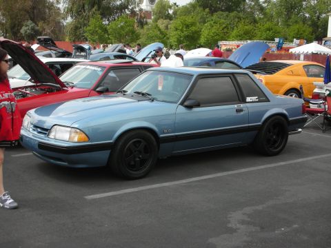 1992 Ford Crown Victoria - Blue coupe with black wheels and "BOTIC" sticker on the rear quarter window, parked at an outdoor car show.