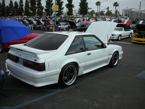 1992 Ford Crown Victoria - A white coupe with a spoiler and aftermarket wheels is parked at a car show.