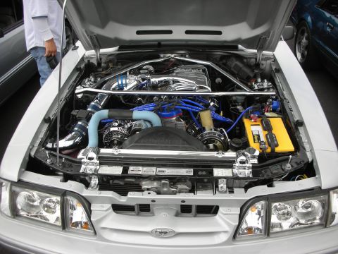 1992 Ford Crown Victoria - Engine bay of a silver 1993 Ford Mustang, modified with chrome and blue components.