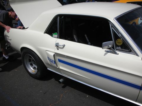 1992 Ford Crown Victoria - A white 1967 Ford Mustang GT/CS with blue racing stripes is parked outdoors, with its trunk open.