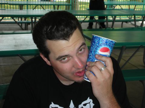 1992 Ford Crown Victoria - A man holds a Pepsi cup to his ear while sitting at a picnic table outdoors.